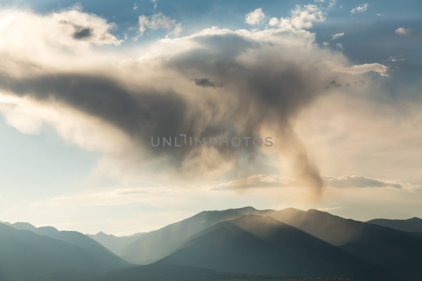 Rain with falling rain spout over the mountains of Colorado with the sun illuminating the falling raindrops on the summit