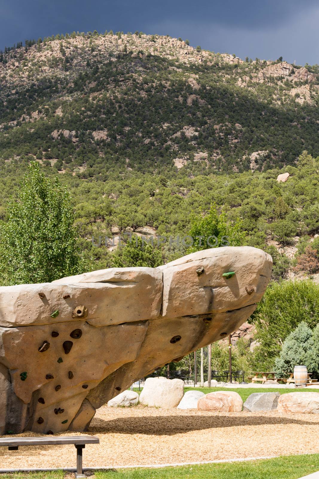 Climbing wall with hand holds and bolted fasteners with real mountain and rocks in the background