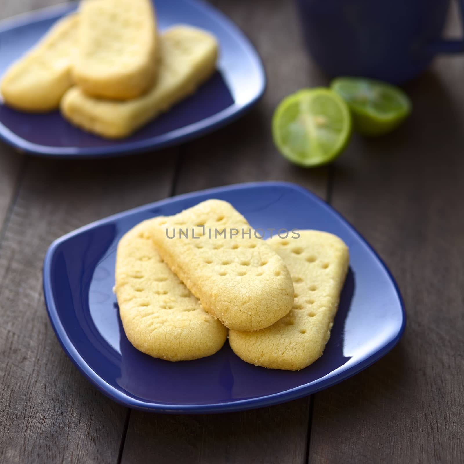 Homebaked shortbread biscuits on small plates with cup of tea in the back (Selective Focus, Focus on the front of the upper shortbread)