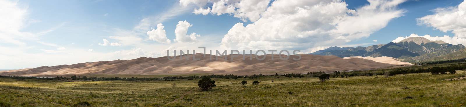 Wide high resolution stitched panorama of the dunes at Great Sand Dunes National Park in Colorado with the mountains behind. Unusual to see clouds over the sand