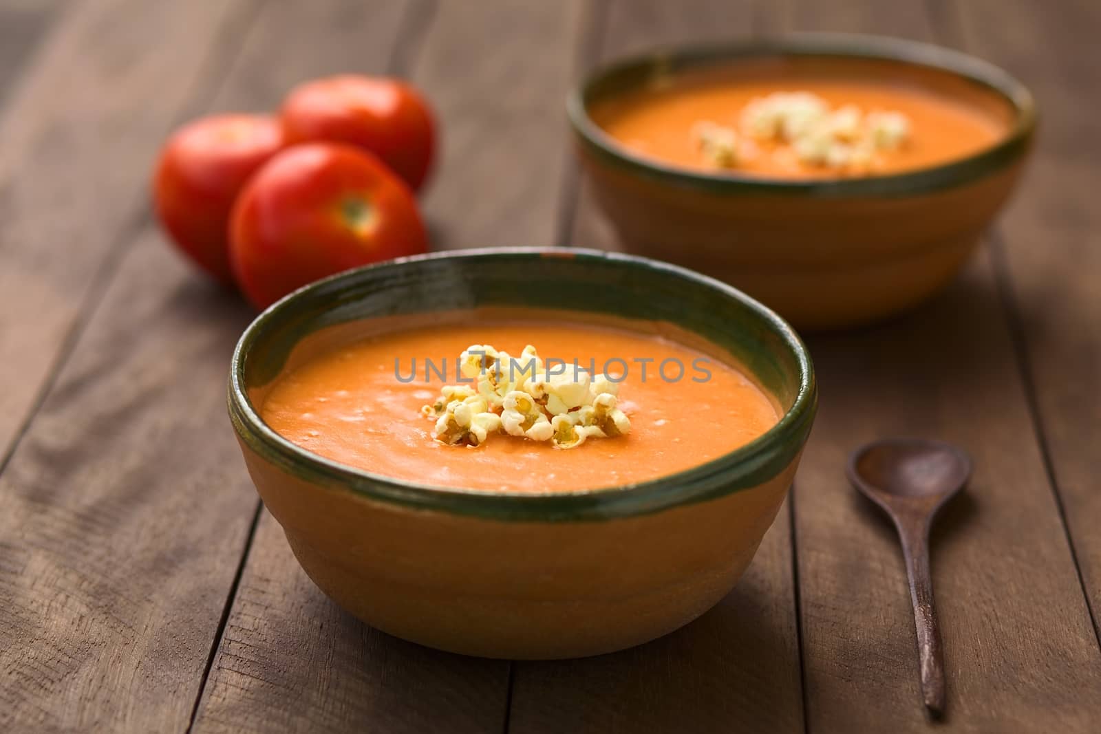 Ecuadorian tomato and potato cream soup served with popcorn on top in rustic bowls (Selective Focus, Focus on the front of the popcorn on the soup)