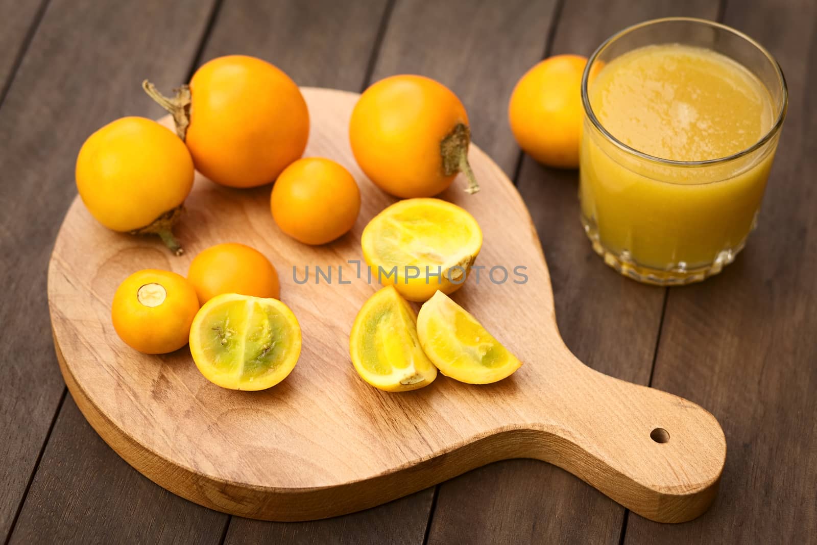 Naranjilla or Lulo fruits (lat. Solanum quitoense) on wooden board with freshly prepared naranjilla juice on the side (Selective Focus, Focus on the cut naranjillas in the front) 