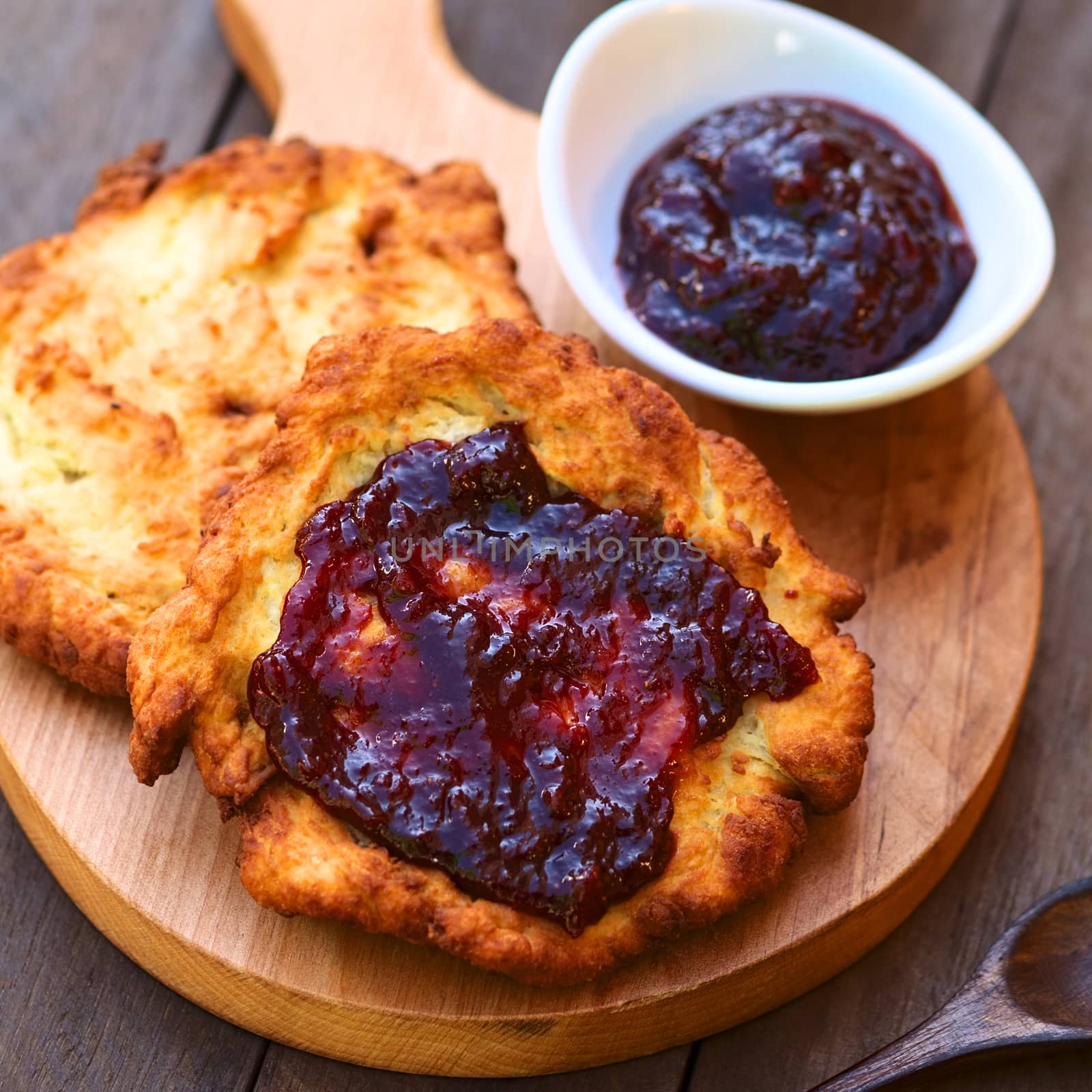 Freshly prepared traditional Hungarian deep fried flat bread called Langos made of a yeast dough, with jam spread on top  (Selective Focus, Focus in the middle of the langos) 

 