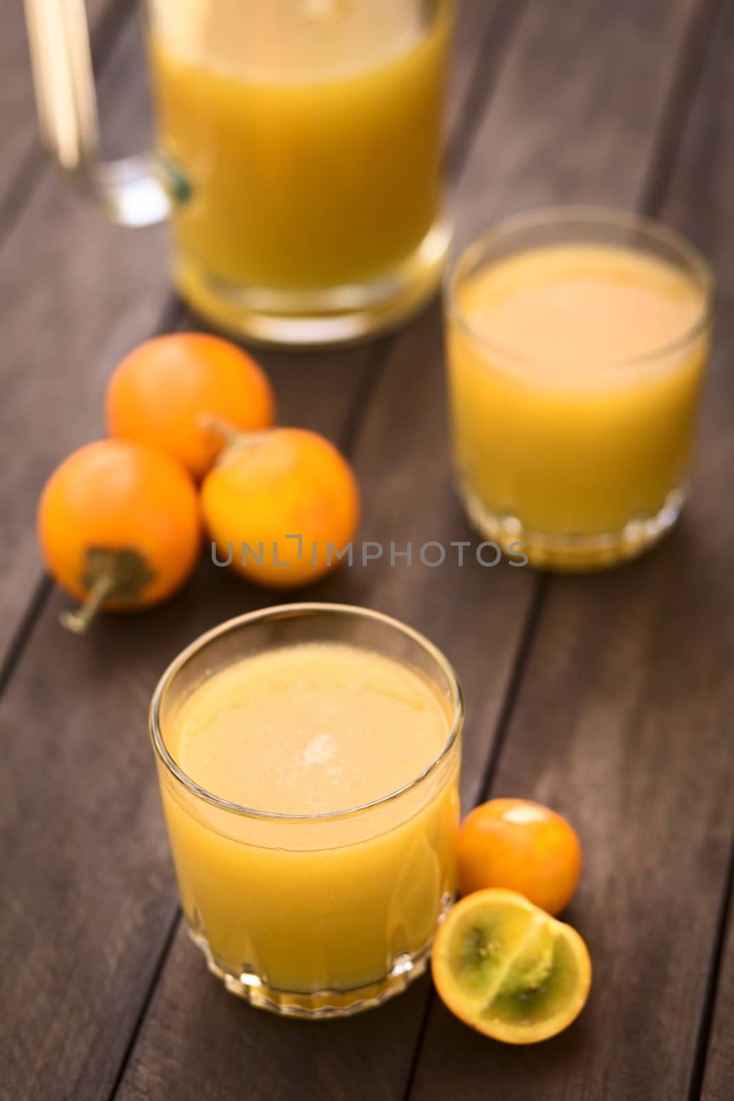 Freshly prepared juice out of Naranjilla or Lulo fruits (lat. Solanum quitoense) with fruits on the side and in the back (Selective Focus, Focus on the front rim of the glass) 