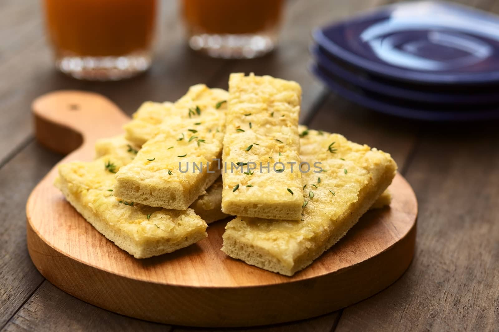 Fresh homemade garlic and cheese sticks made of a yeast dough served on wooden board, sprinkled with fresh thyme leaves (Selective Focus, Focus one third into the upper garlic stick)