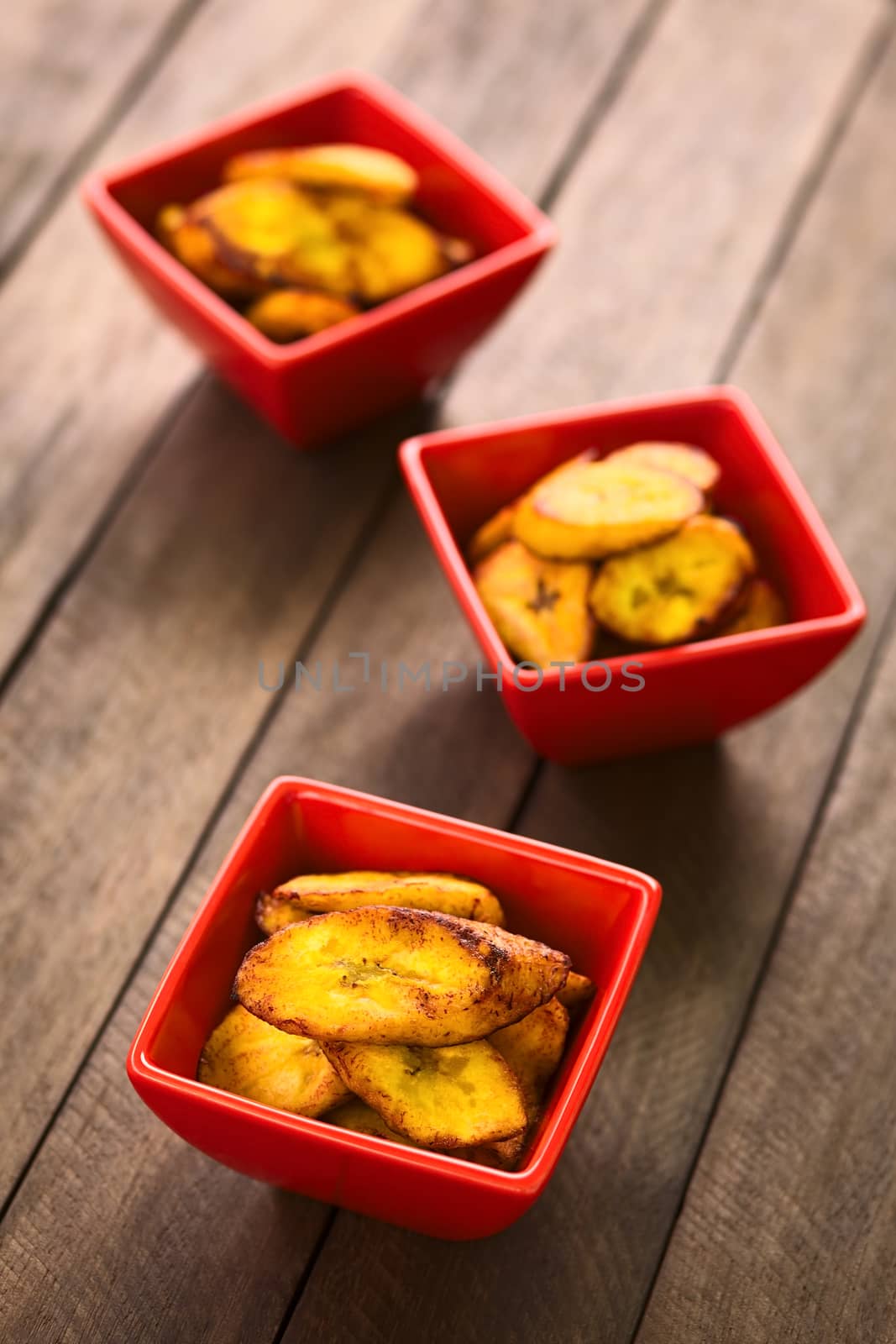 Fried slices of the ripe plantain in small red bowls, which can be eaten as snack or is used to accompany dishes in some South American countries (Selective Focus, Focus on the front of the upper plantain slice in the first bowl)