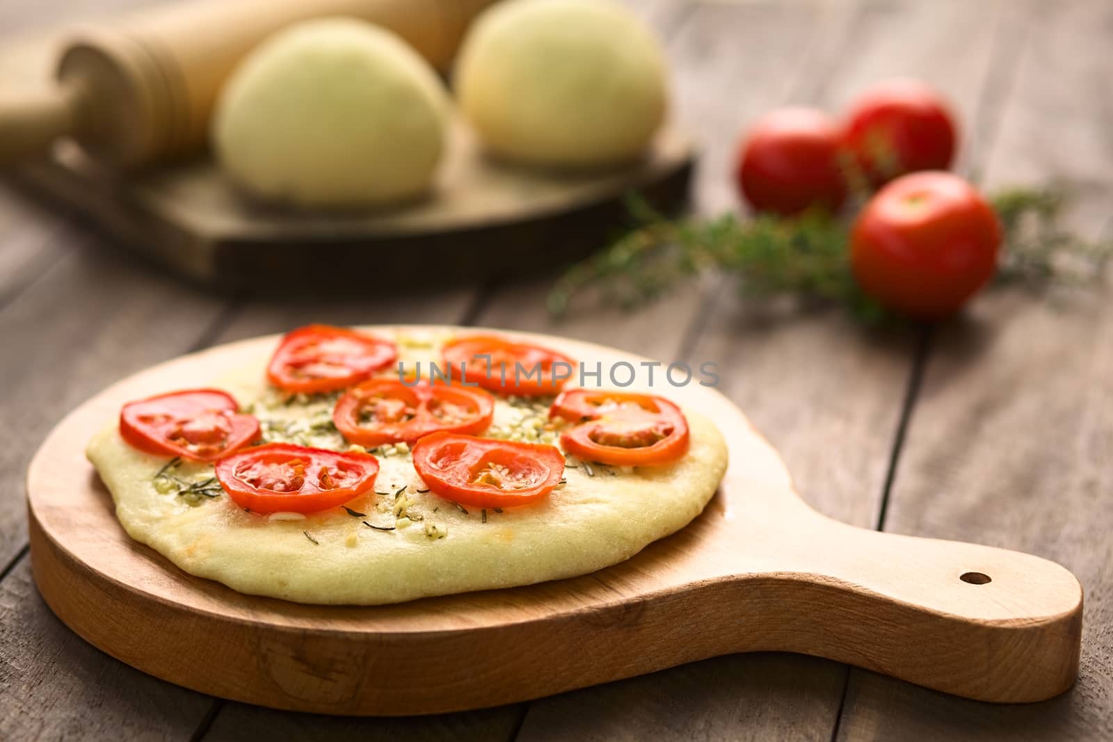 Freshly baked homemade yeast-dough flatbread topped with tomato slices, garlic and thyme leaves served on wooden board (Selective Focus, Focus on the front of the first tomato slices)  