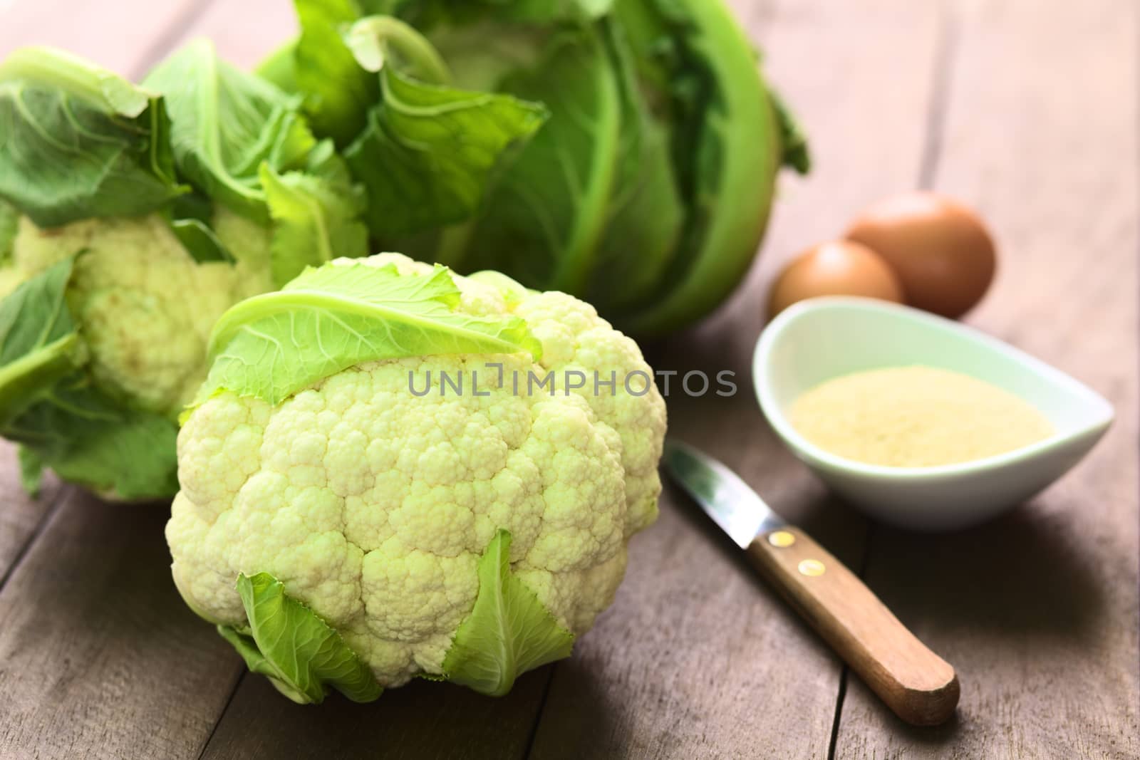 Raw cauliflower with breadcrumbs and eggs in the back for breading (Selective Focus, Focus on the front of the cauliflower) 