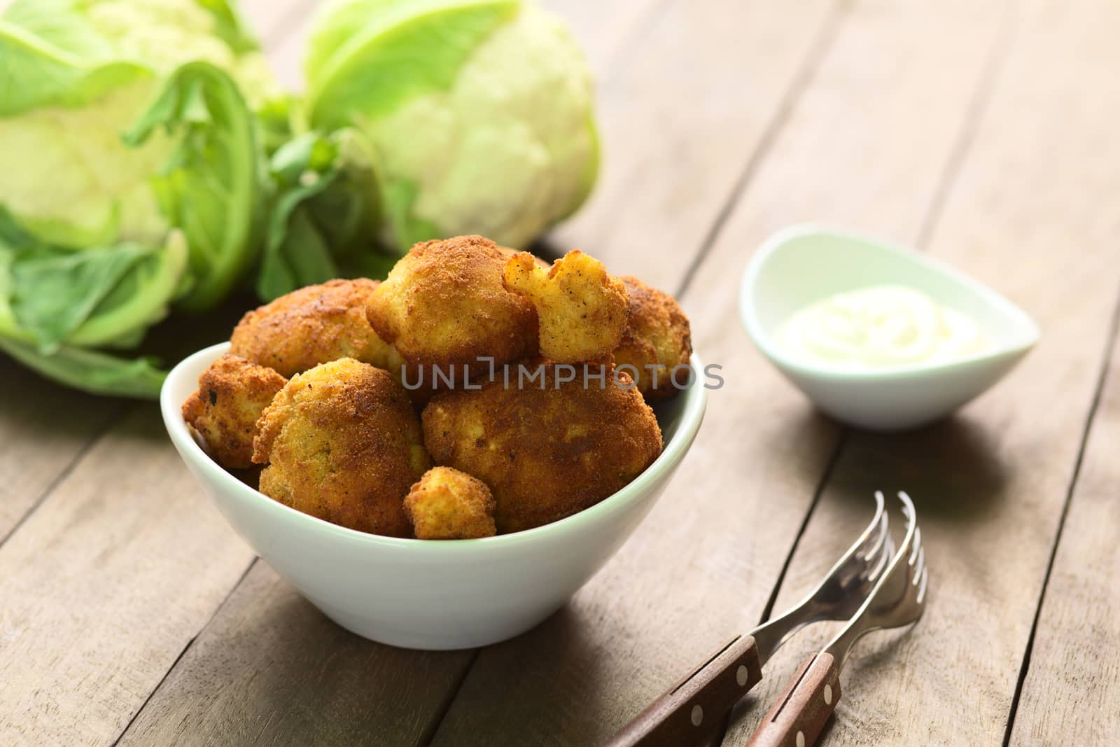 Freshly prepared breaded cauliflower in bowl with mayonnaise to dip and raw cauliflower in the back (Selective Focus, Focus on the front of the top cauliflower heads in the bowl)