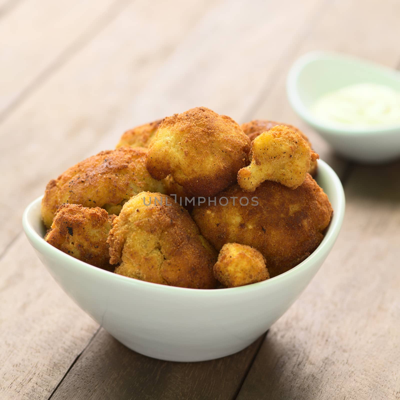 Freshly prepared breaded cauliflower in bowl with mayonnaise to dip in the back (Selective Focus, Focus on the front of the top cauliflower heads)