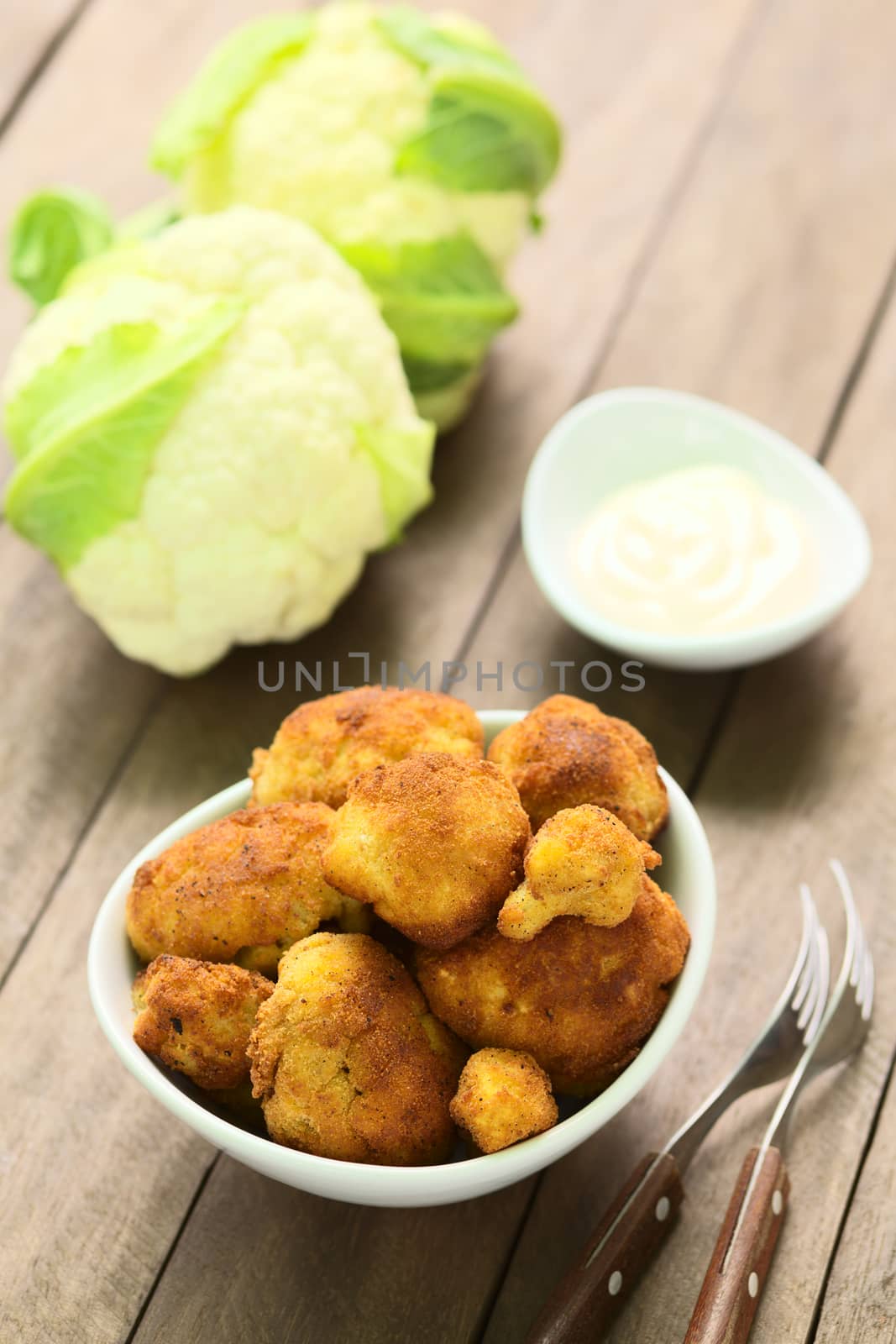 Freshly prepared breaded cauliflower in bowl with mayonnaise to dip and raw cauliflower in the back (Selective Focus, Focus on the front of the top cauliflower heads in the bowl)