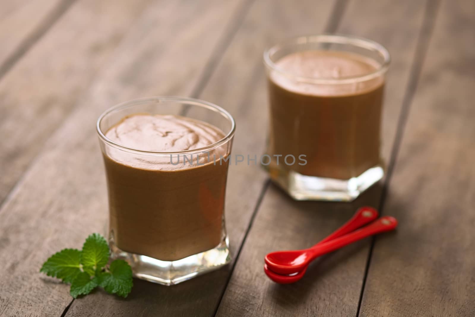 French dessert called Mousse au Chocolat, made of melted chocolate, egg, cream and sugar served in glasses with two small spoons on the side (Selective Focus, Focus on the front rim of the first glass)