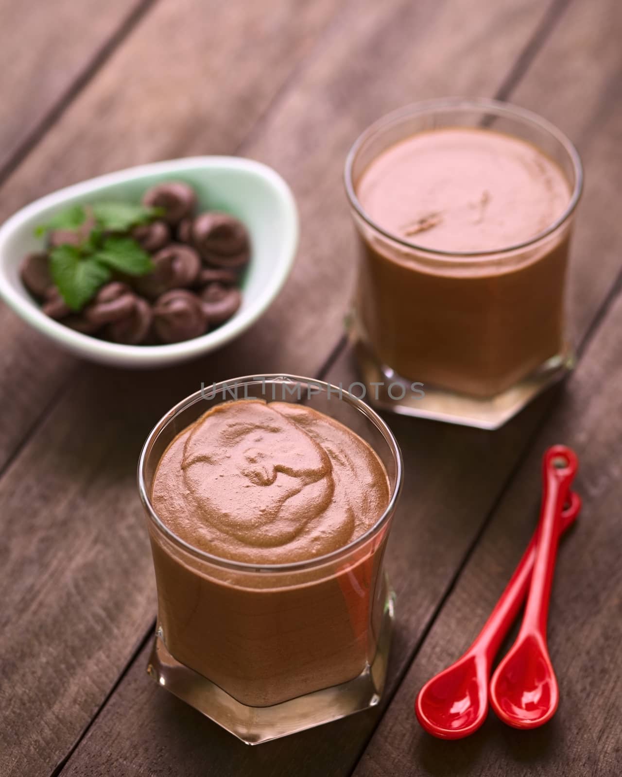 French dessert called Mousse au Chocolat, made of melted chocolate, egg, cream and sugar served in glasses with two small spoons on the side (Selective Focus, Focus onto the middle of the first dessert)