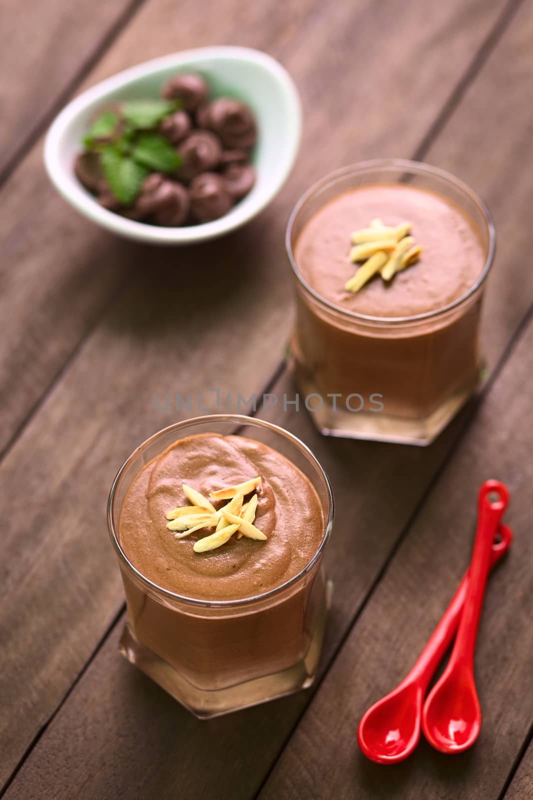 French dessert called Mousse au Chocolat, made of melted chocolate, egg, cream and sugar served in glasses and garnished with roasted almond pieces (Selective Focus, Focus on the front of the almond pieces on the first dessert)