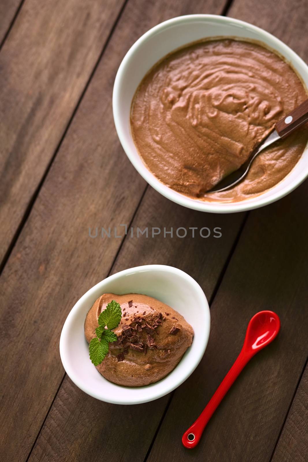 French dessert called Mousse au Chocolat, made of melted chocolate, egg, cream and sugar served in small bowl and garnished with grated chocolate and lemon balm leaf (Selective Focus, Focus onto the dessert in the small bowl)