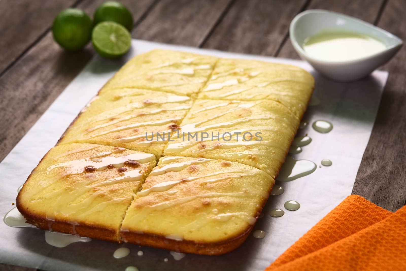 Fresh homemade key lime cake with lime icing on top on parchment paper with lime icing and key limes in the back (Selective Focus, Focus one third into the cake)