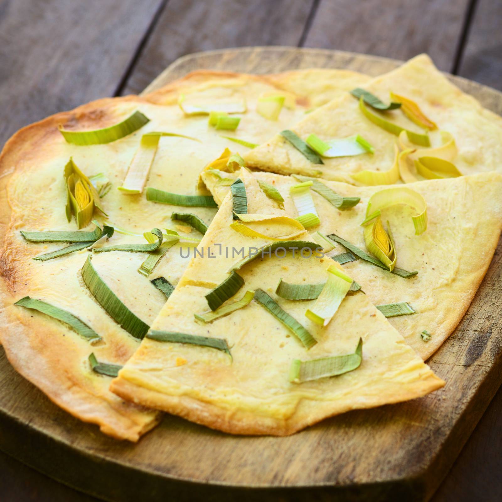 French vegetarian Tarte Flambee made of thin bread dough with a cream and leek topping, served on wooden board (Selective Focus, Focus on the upper part of the first piece)  