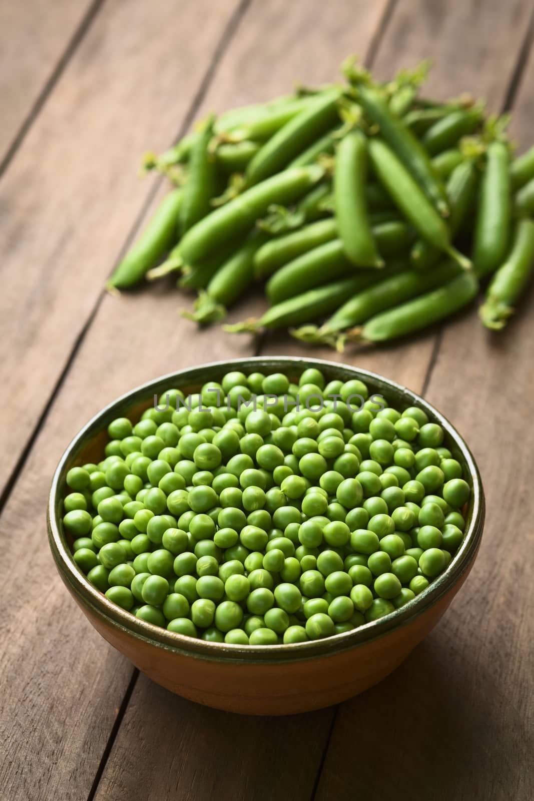 Peas (lat. Pisum sativum) in bowl with closed peapods in the back (Selective Focus, Focus into the middle of the peas)