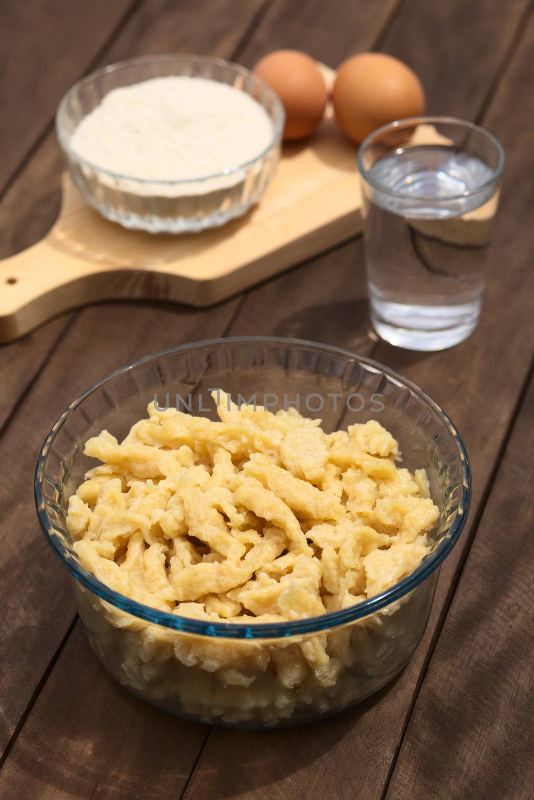 Glass bowl with homemade Hungarian Nokedli or Galuska, a type of egg noddle, made by cutting the soft dough on a wooden board into boiling water (Selective Focus, Focus into the middle of the noodles) 
 