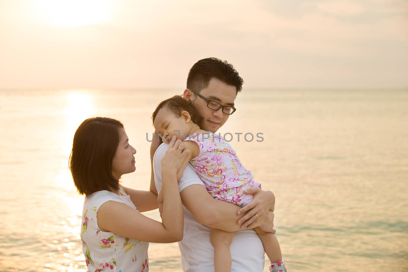 Portrait of young Asian family outdoor beach vacation, during summer sunset, natural sunlight. 