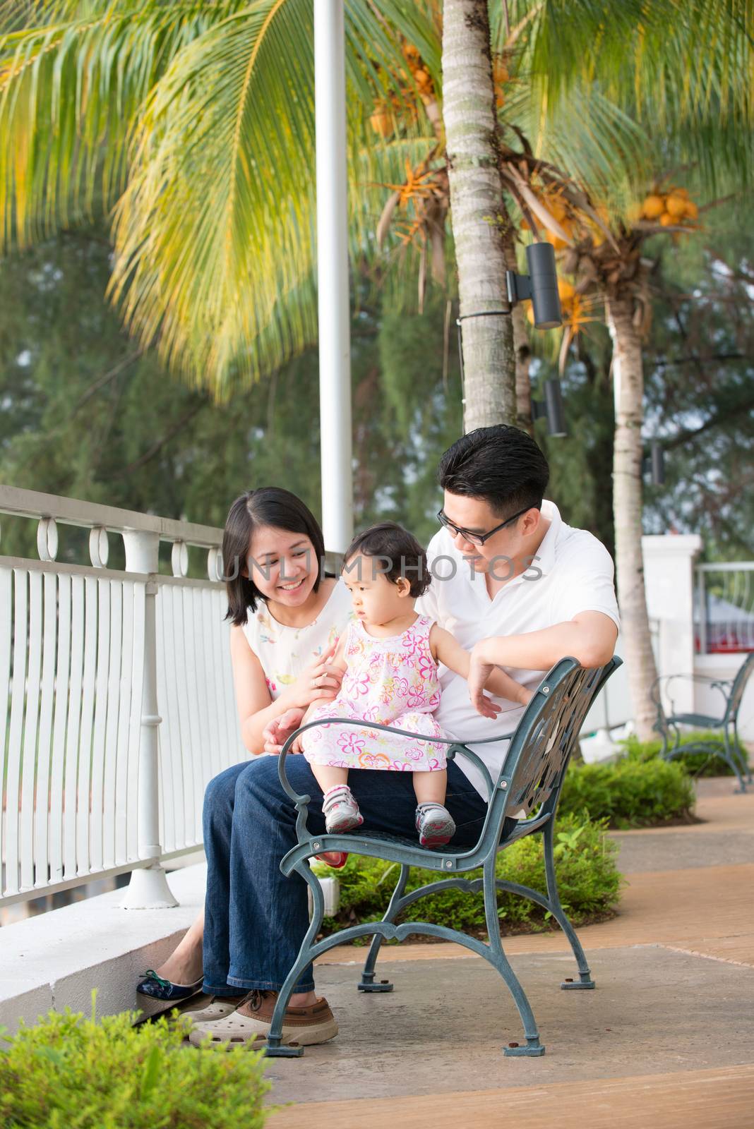 Happy Asian family portrait sitting at outdoor bench.