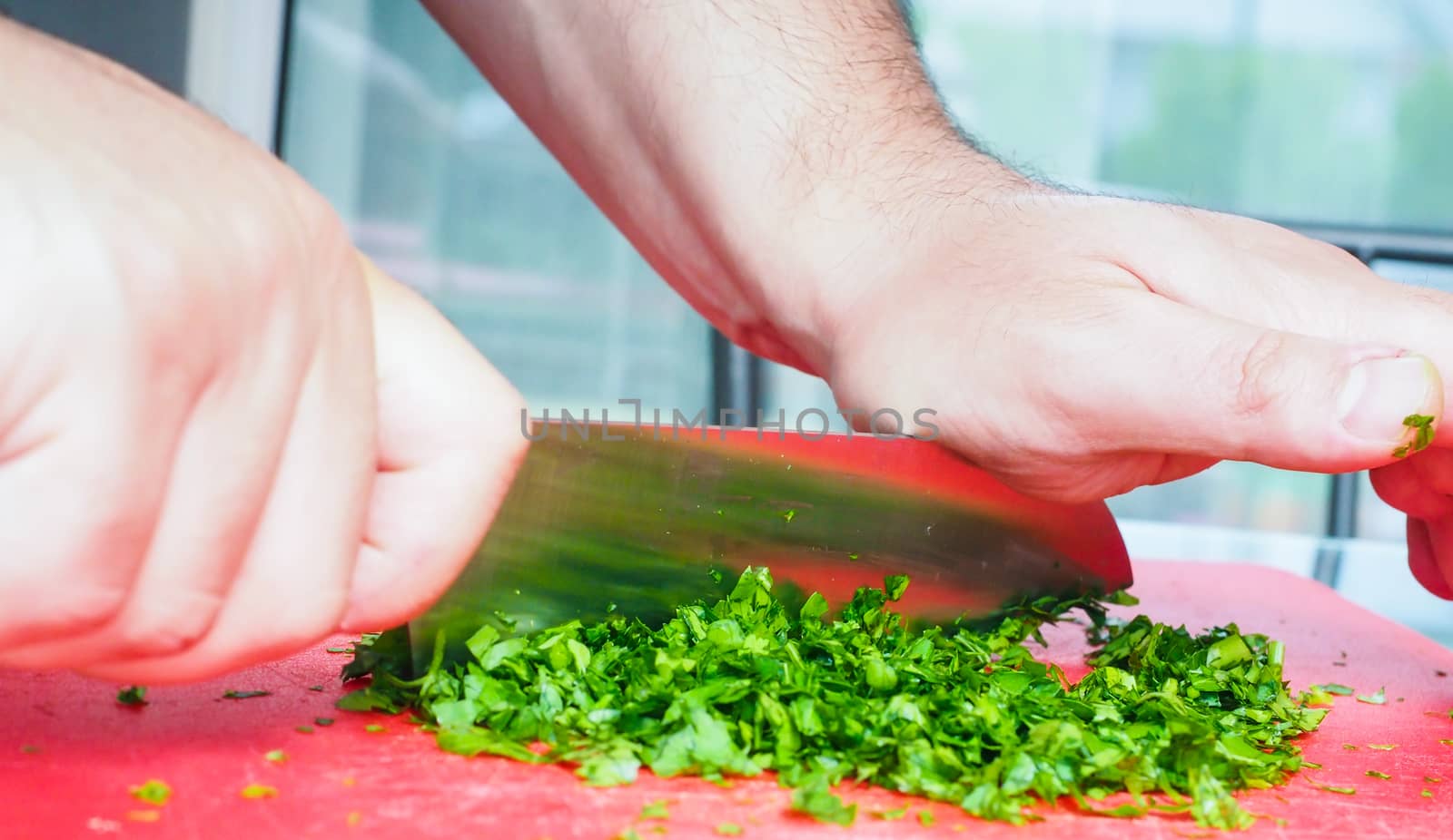 Male chef cutting parsley with big knife on red chopping board by Arvebettum