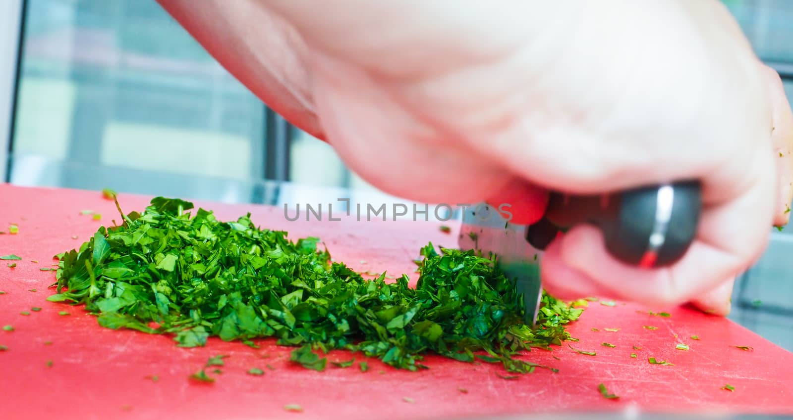 Male chef cutting parsley with big knife on red chopping board by Arvebettum