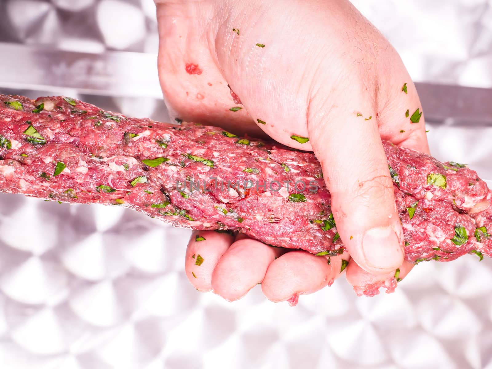 A chef making shish kebab of red meat with parsley over metal plate