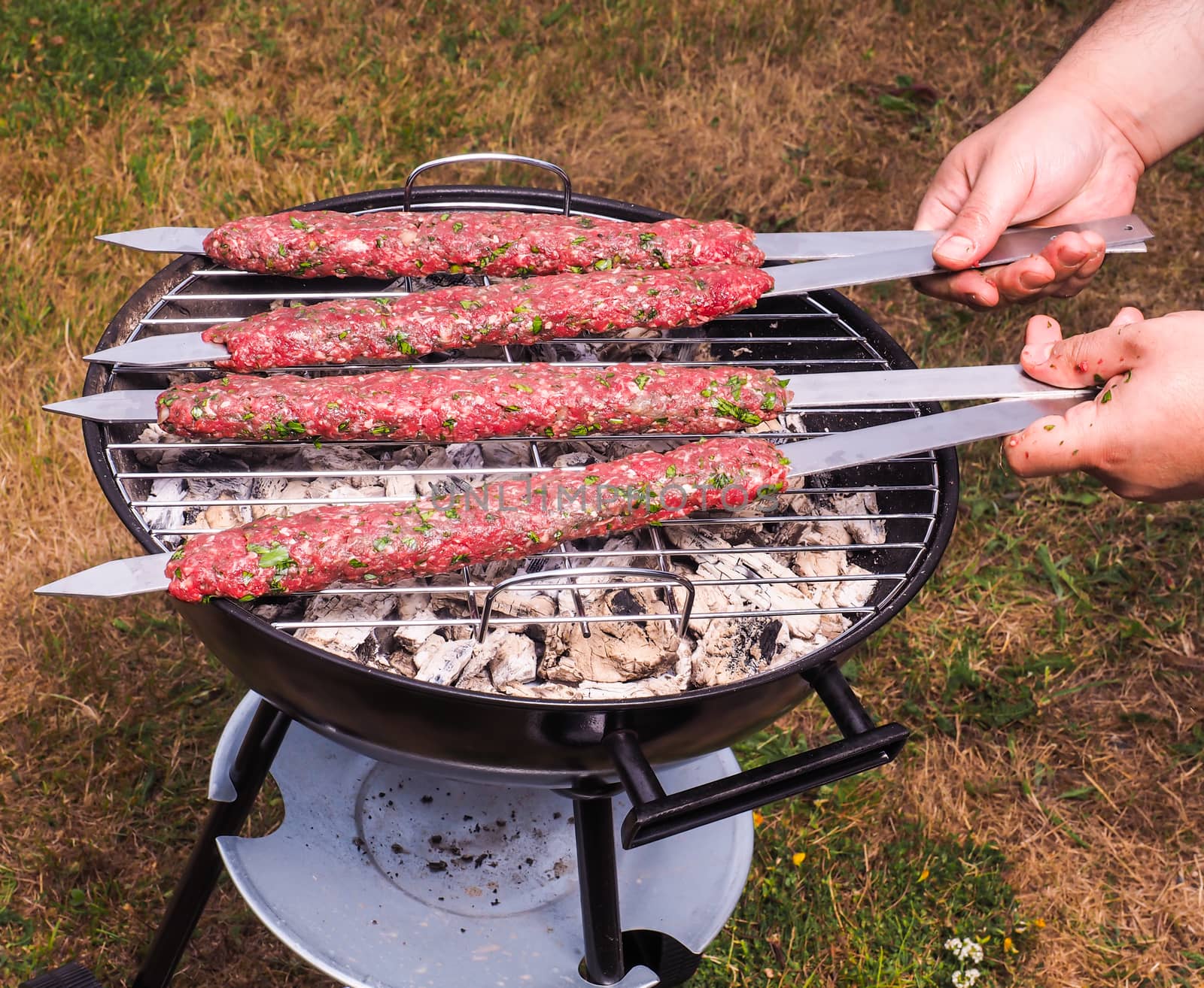 A chef putting red meat shish kebab onto a charcoal barbecue