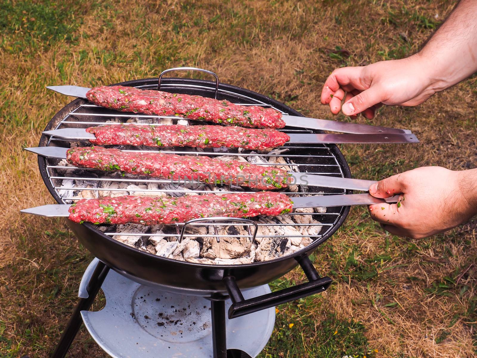 A chef putting red meat shish kebab onto a charcoal barbecue