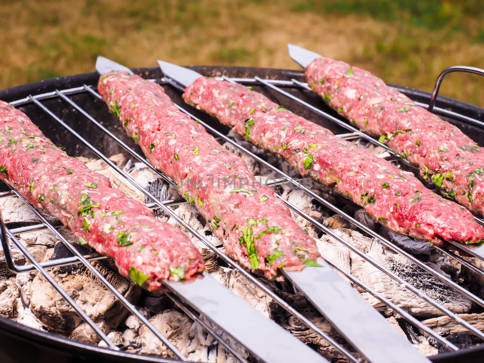 Shish kebab prepared over a black round shaped charcoal barbecue by Arvebettum