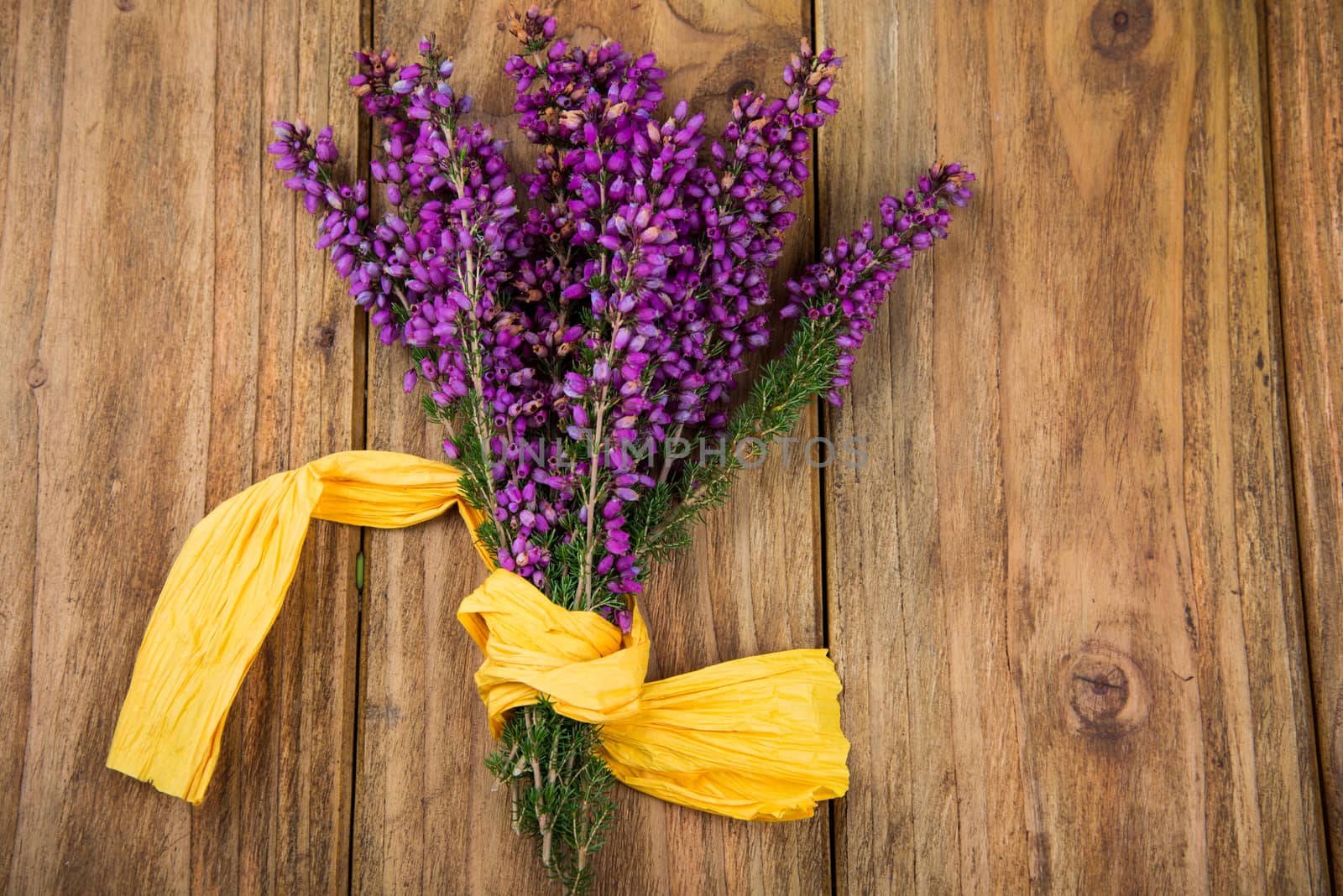 Purple and viola heather flowers on wooden table with yellow ribbon