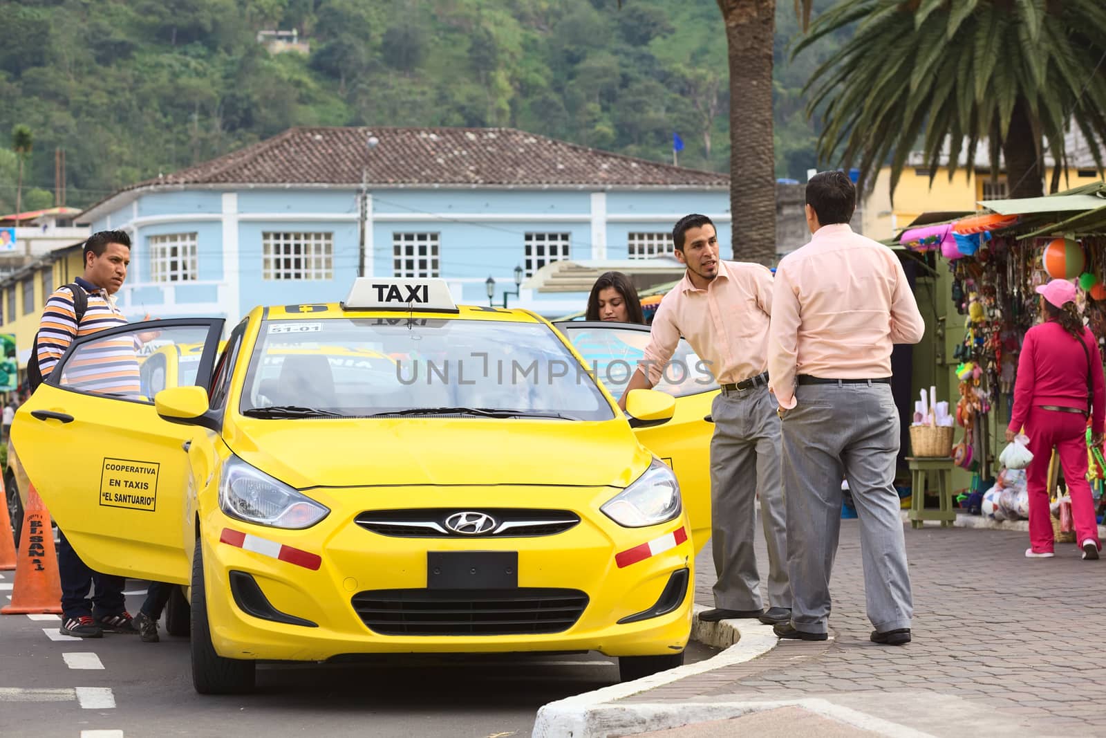 BANOS, ECUADOR - FEBRUARY 22, 2014: Unidentified taxi drivers talking at taxi stand on 12 de Noviembre Street outside the cathedral while passengers are getting into the car on February 22, 2014 in Banos, Ecuador.