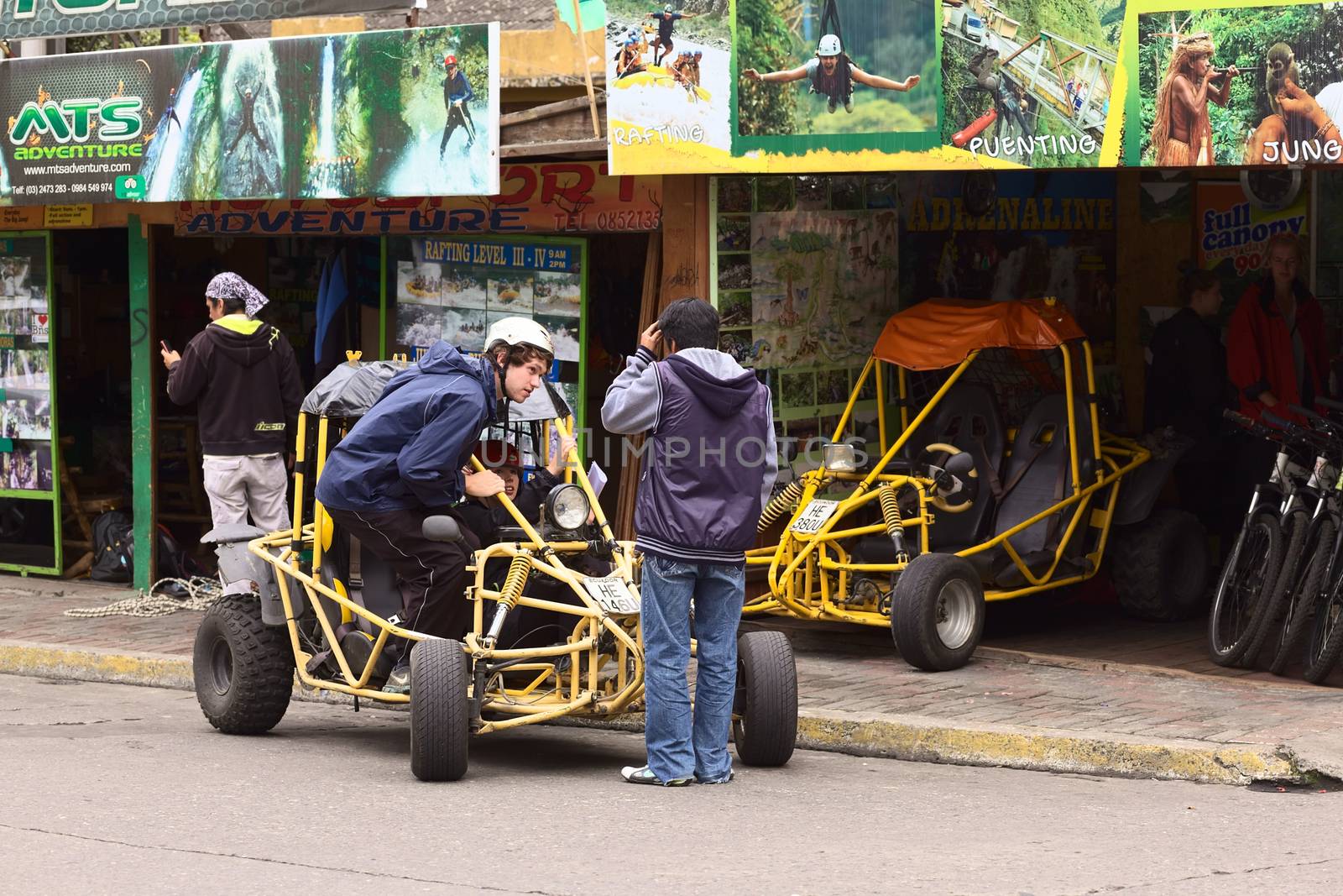 BANOS, ECUADOR - FEBRUARY 25, 2014: Unidentified people in and at a buggy in front of a tour operator and vehicle rental on 16 de Diciembre Street on February 25, 2014 in Banos, Ecuador. Banos is a small touristy town, which is mainly visited for its outdoor activities, such as bridge jumping, canyoning, kayaking, and so on. There are also various places to rent bikes, buggies and quads. 