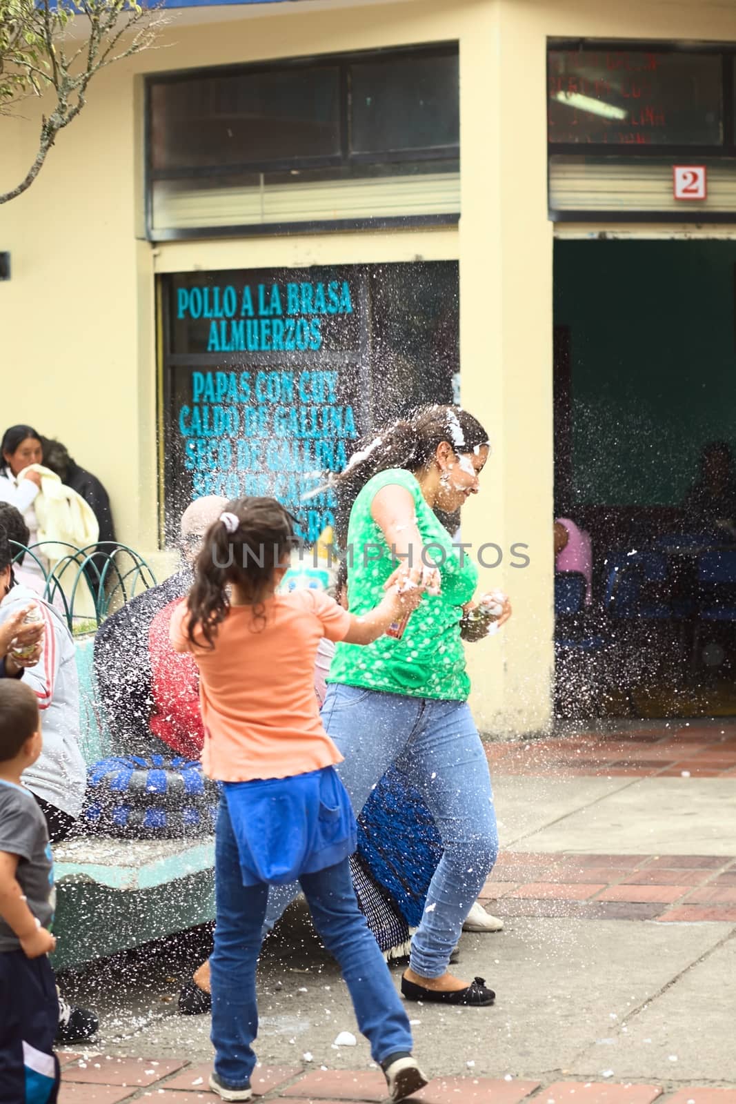 BANOS, ECUADOR - MARCH 2, 2014: Unidentified young woman being sprayed with foam at carnival on Ambato Street on March 2, 2014. It is officially forbidden to use foam or water to spray others, but still many are using the sprays and it is being sold in many shops. (Selective Focus, Focus on the woman in green t-shirt)