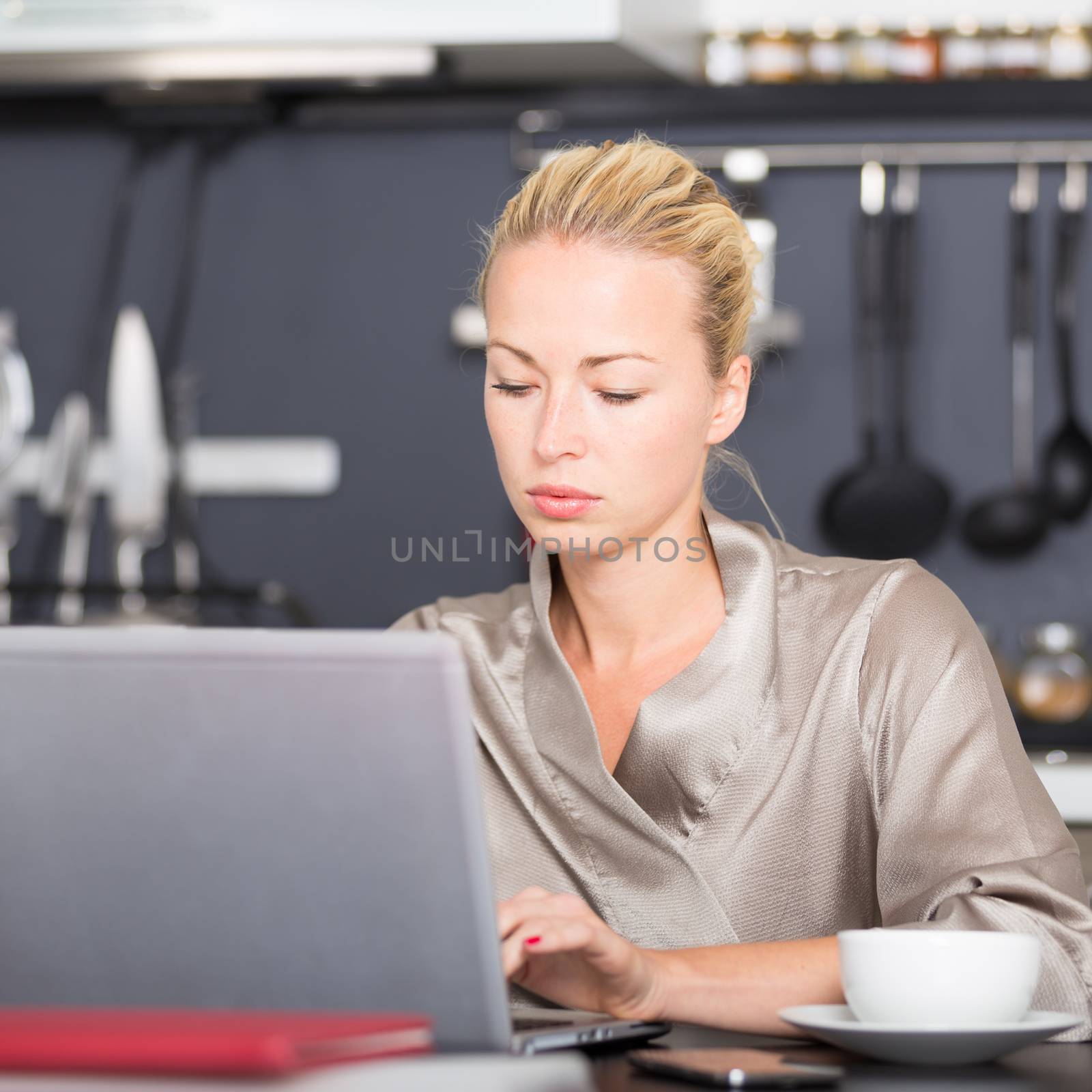 Business woman in her nightgown working remotly from her dining table in the morning. Home kitchen in the background.