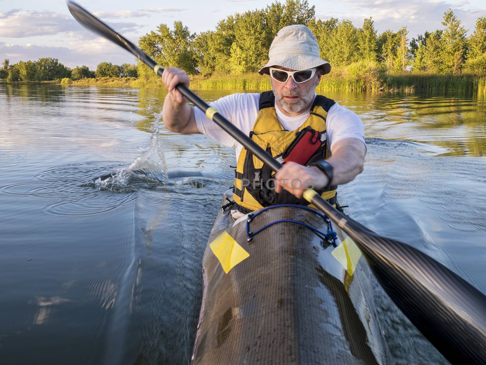 senior male paddler training in a fast sea kayak by PixelsAway