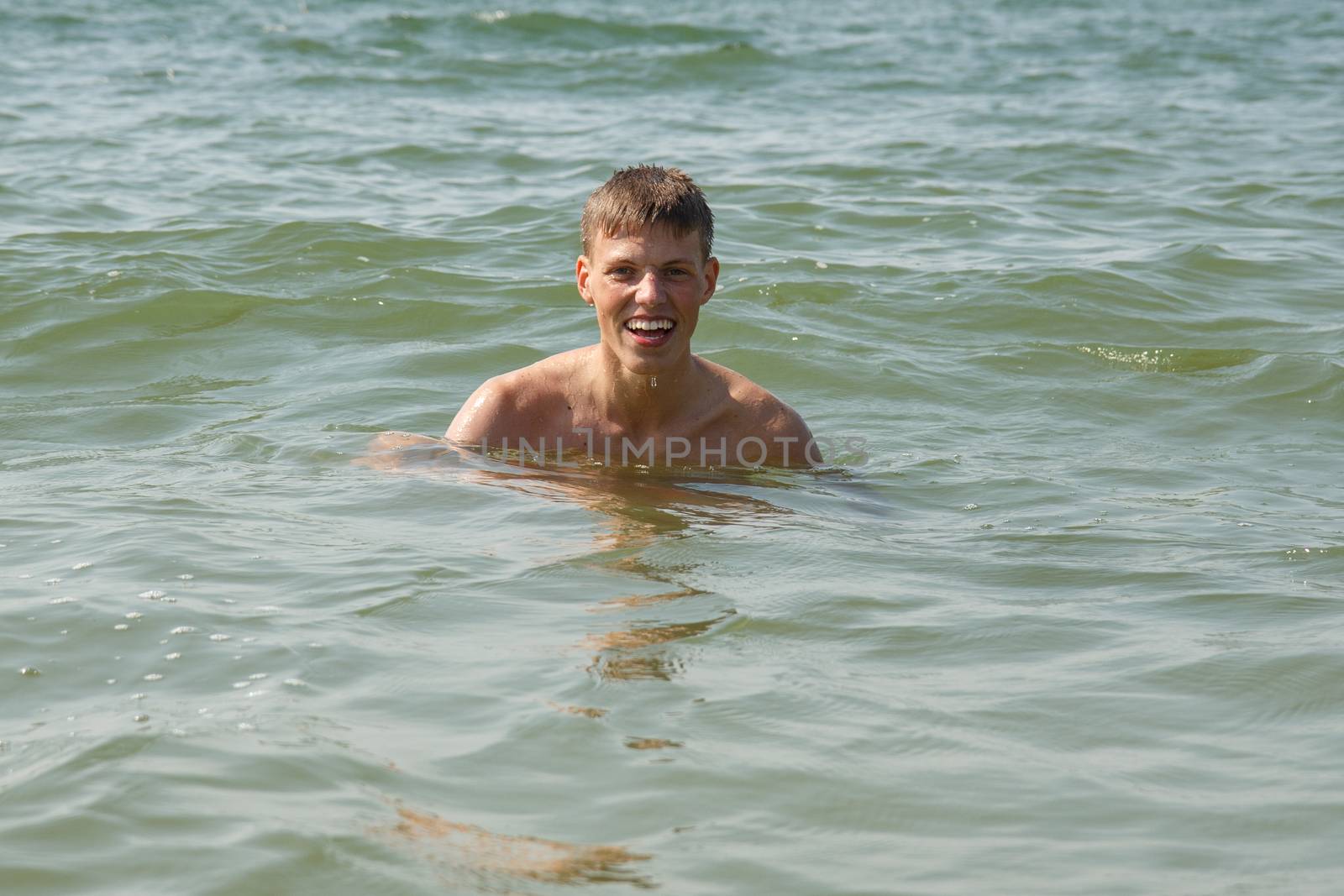 A boy swimming and smiling at the beach