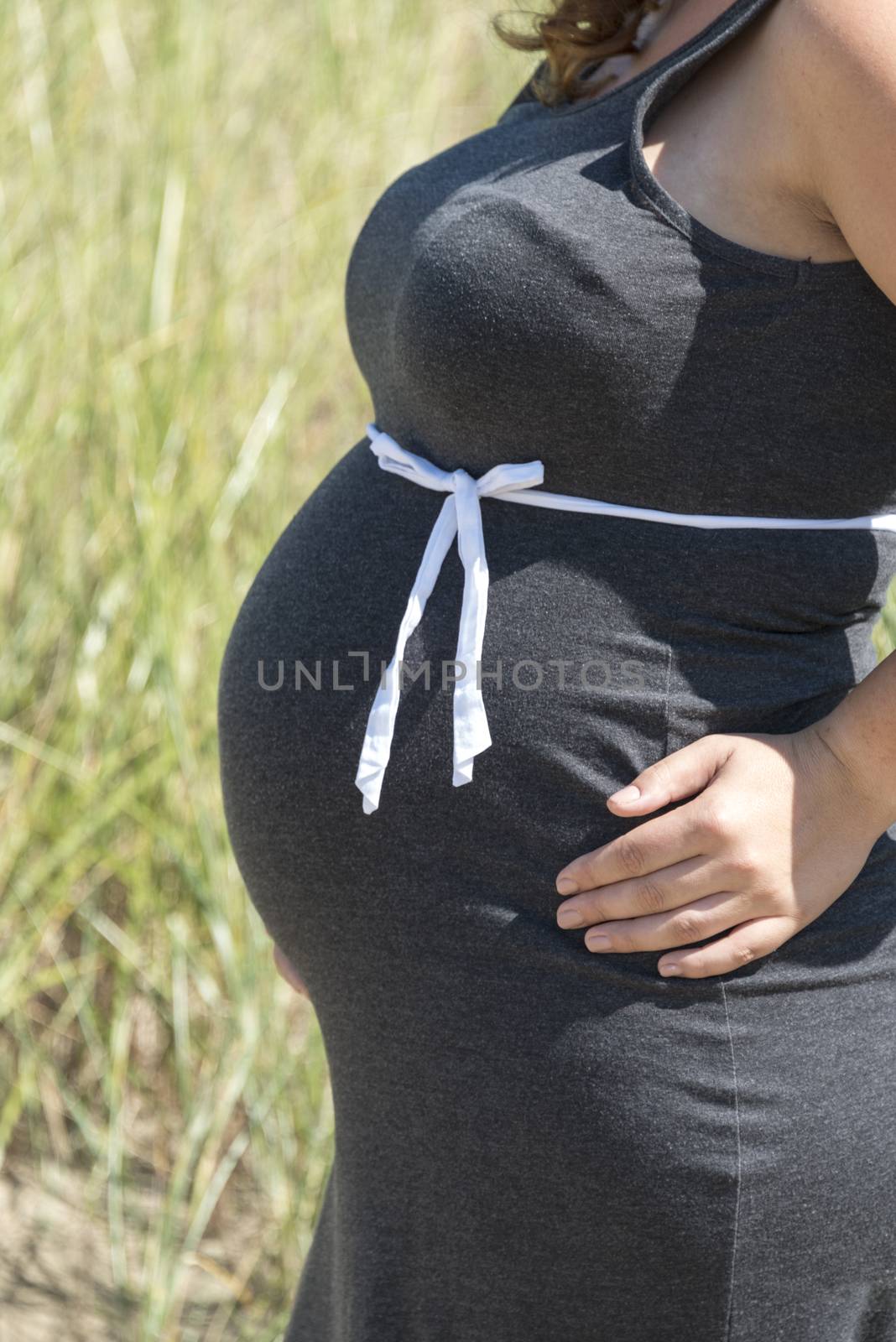 pregnant woman with white bow on here belly outside in nature