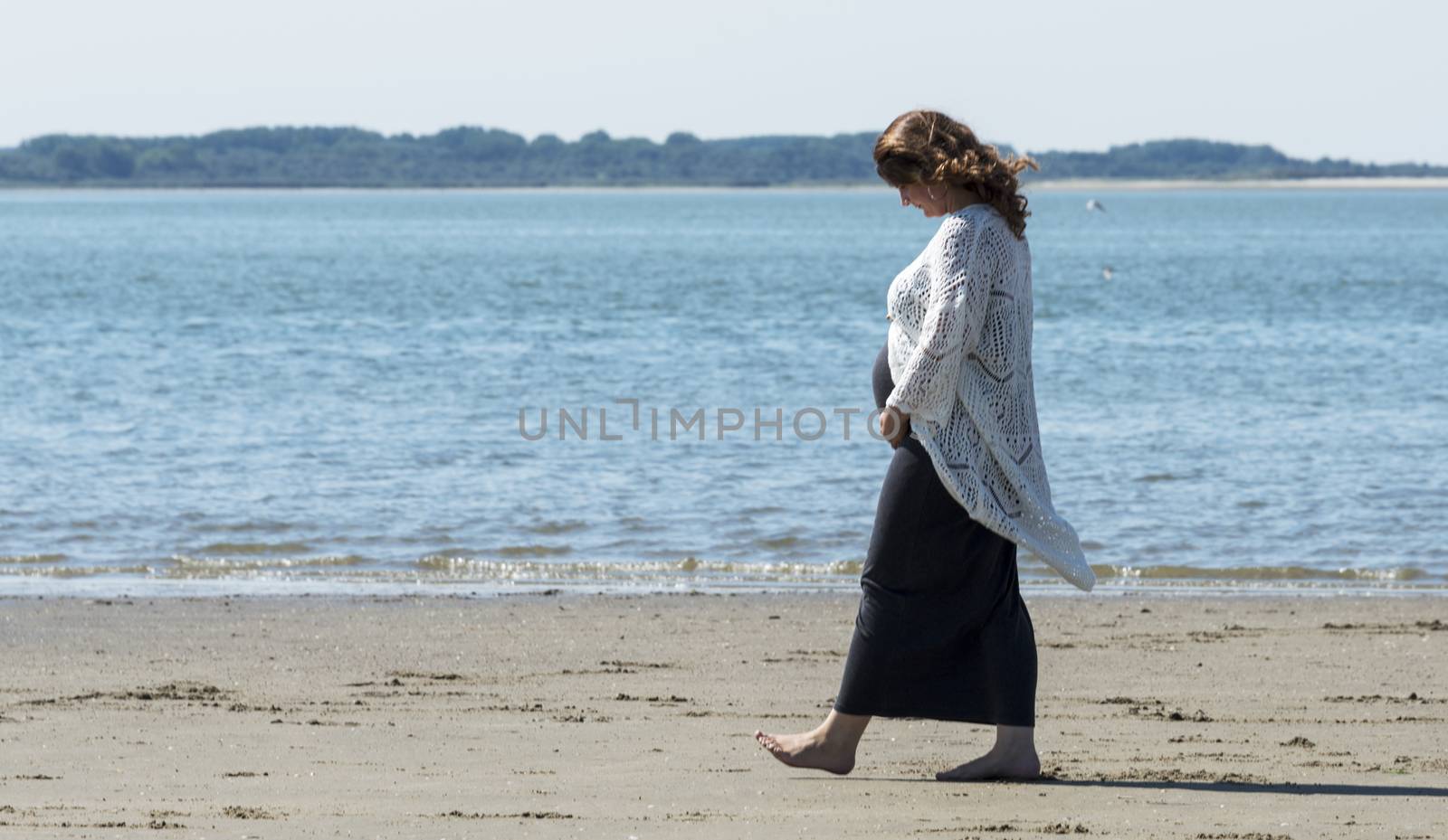 pregnant woman walking on the beach  by compuinfoto