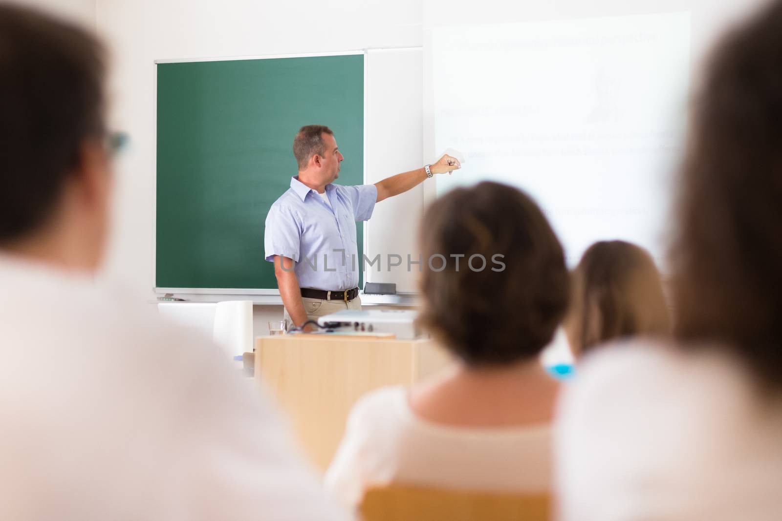 Teacher at university in front of a whiteboard screen. Students listening to lecture and making notes.