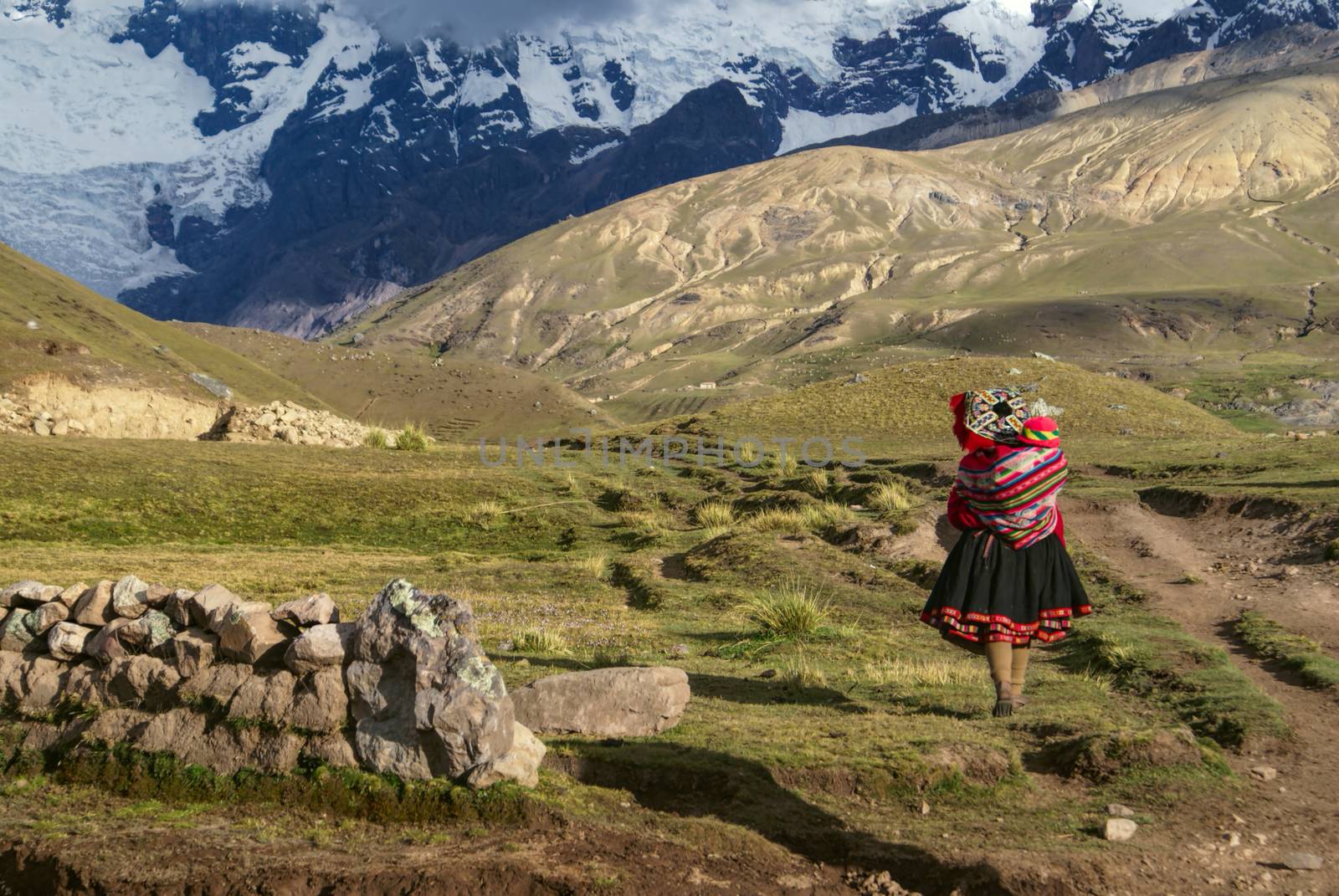 A Peruvian woman walking with a child on her back in South American Andes