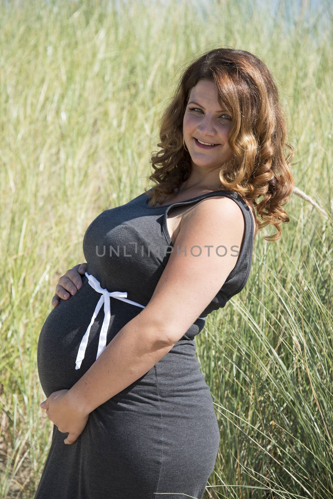 pregnant woman with white ribbon bow on her belly in nature with straw background