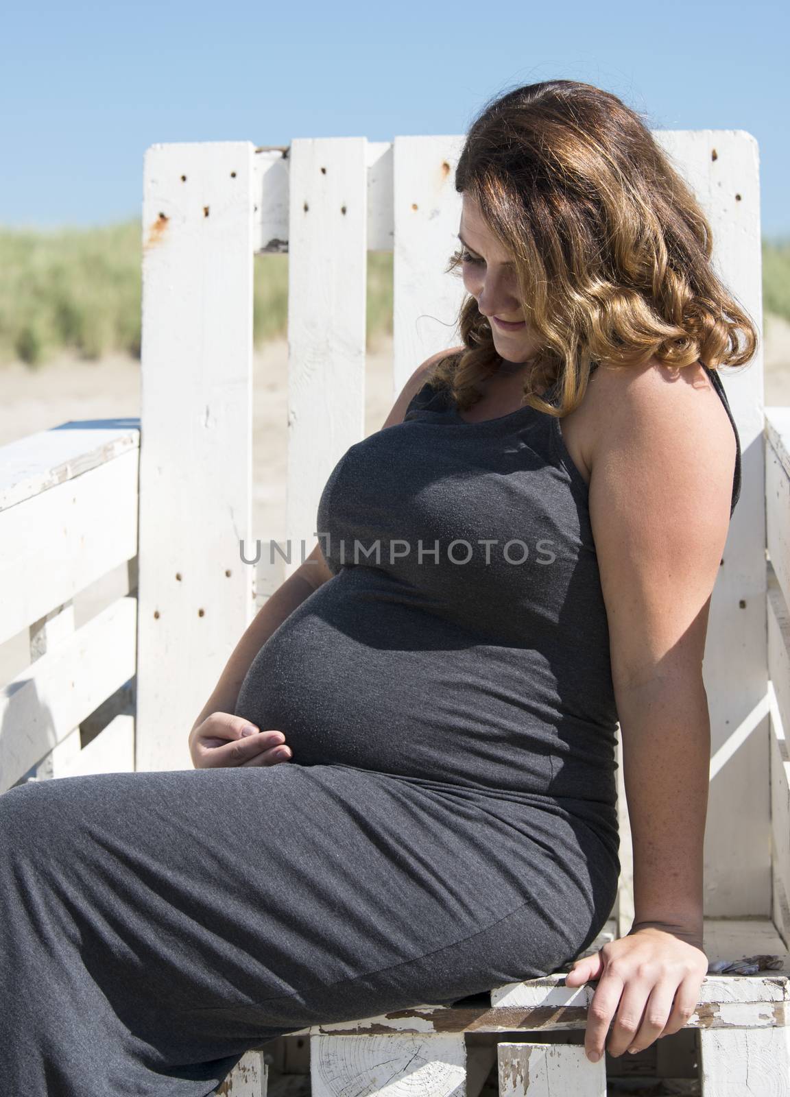 adult happy pregnant woman sitting on wooden chair on the beach