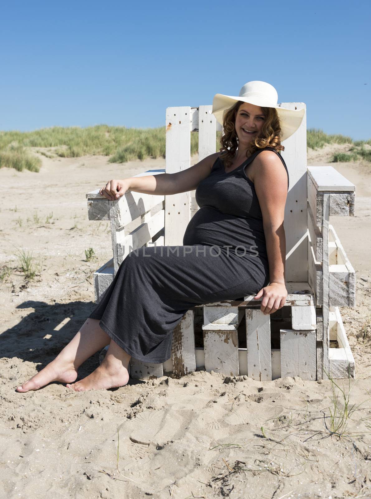 adult happy pregnant woman sitting on wooden chair on the beach