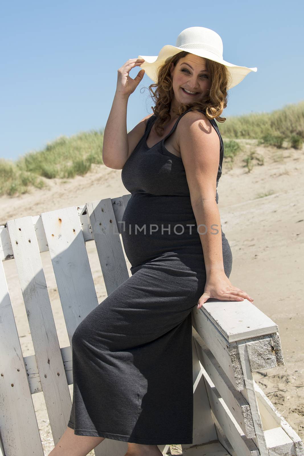 pregnant woman with hat on wooden chair on the beach