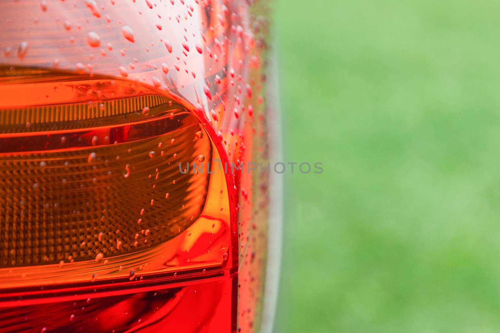 Wet after rain with water drops tail lights of new modern car on fresh green grass