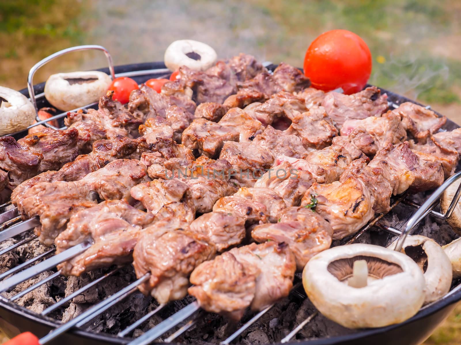 Shish kebab prepared over a black round shaped charcoal barbecue by Arvebettum