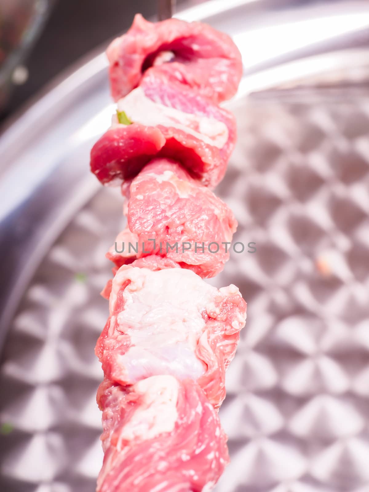 Closeup  of raw meat in sliceses entered on a skewer over metal  by Arvebettum