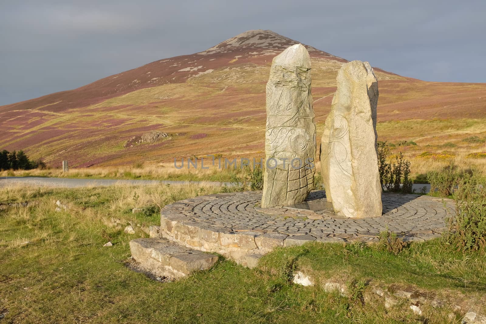 Carved standing stones on a plinth with the heather flanks of Yr Eifl in the distance, Lleyn Peninsular, Gwynedd, Wales, UK.